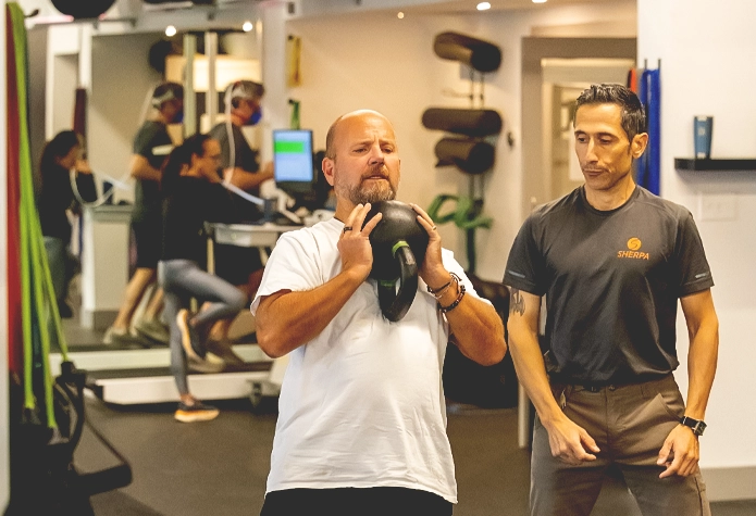 Coach guiding athlete through kettlebell lift during personal training at Sherpa in Westport, CT