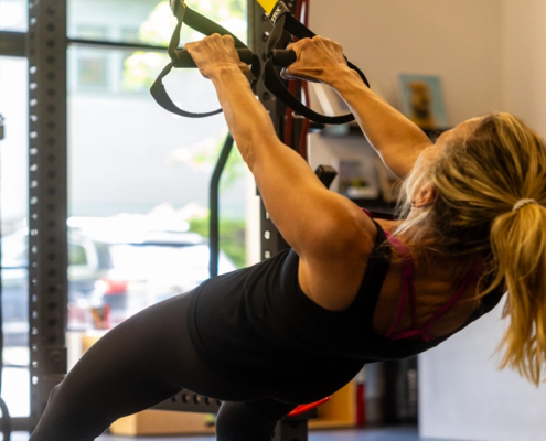 Woman performing suspension trainer pull-ups using bodyweight training straps at Sherpa fitness studio in Westport CT
