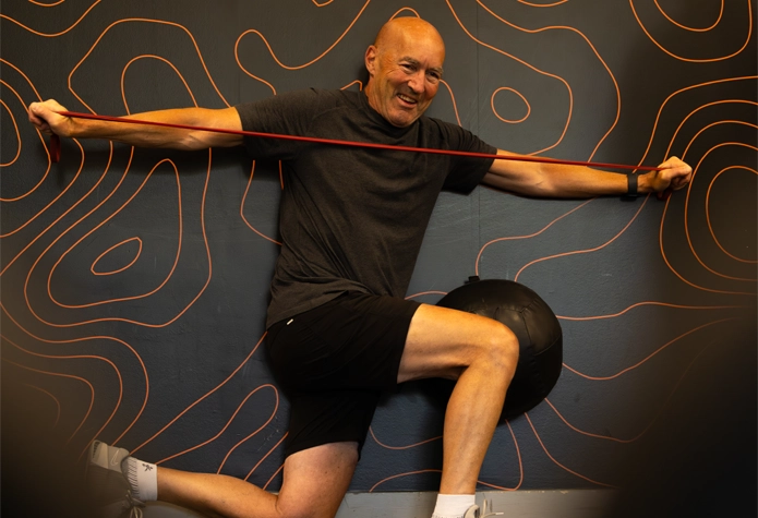 Man performs resistance band mobility work at Sherpa in Westport, CT, in front of the Sherpa brand pattern wall.