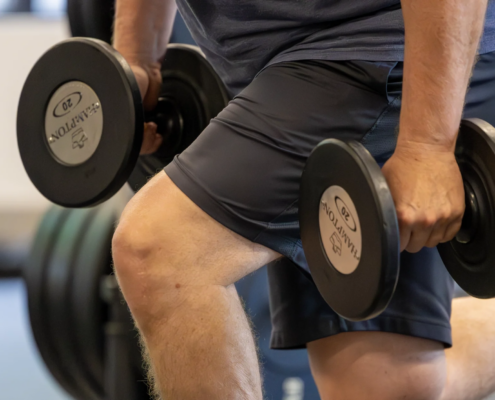Active adult man performing a dumbbell split squat at Sherpa in Westport, CT with front knee bent at 90 degrees and back leg extended behind him