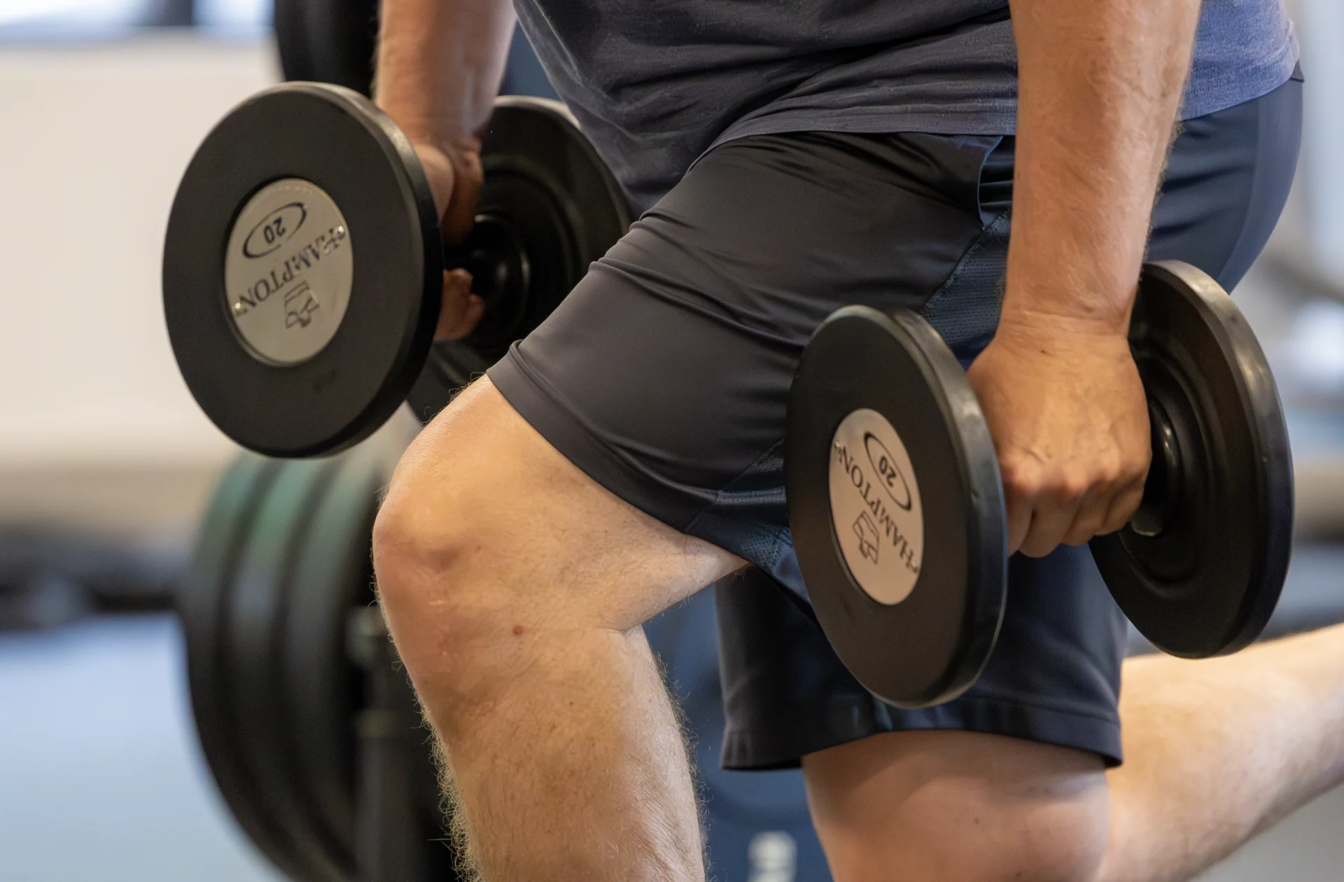 Active adult man performing a dumbbell split squat at Sherpa in Westport, CT with front knee bent at 90 degrees and back leg extended behind him