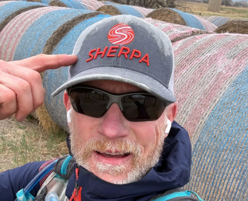 Andy Pemberton pointing at a Sherpa branded hat for a blog about Everest training and goal-specific fitness preparation